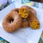 Cinnamon Sugar Pumpkin Donuts stacked on a white plate with cinnamon sugar coating