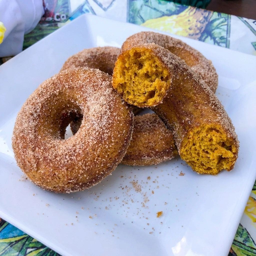 Cinnamon Sugar Pumpkin Donuts stacked on a white plate with cinnamon sugar coating