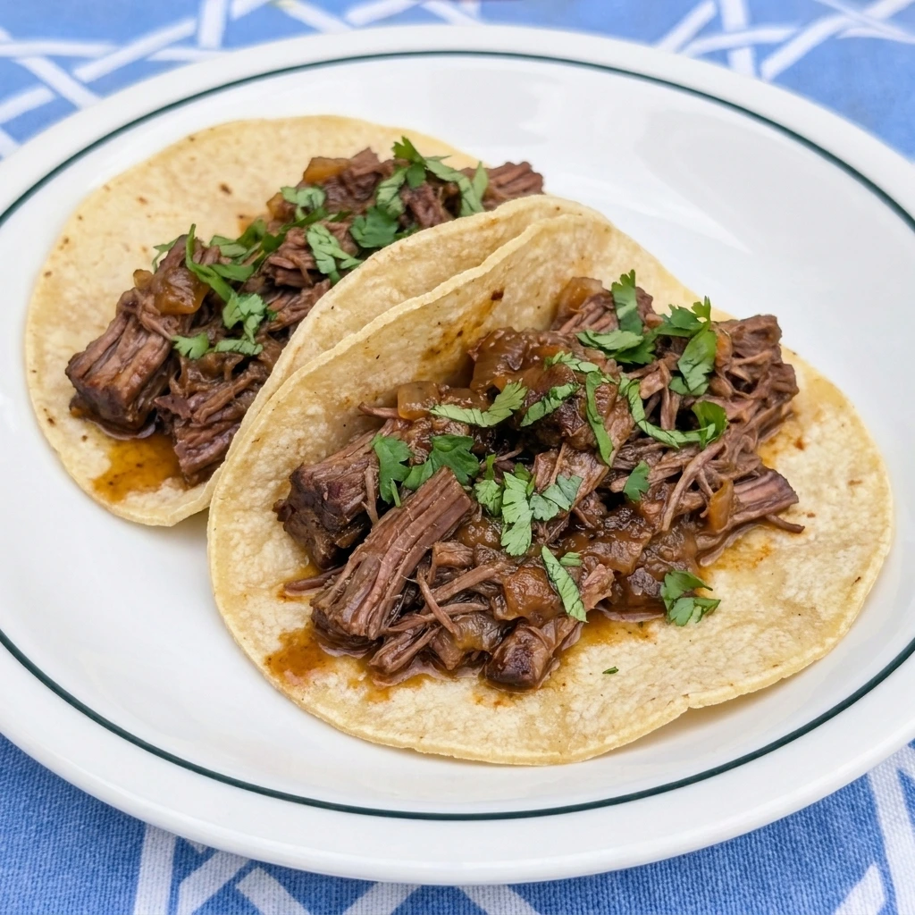 Two Crockpot Barbacoa Beef tacos with cilantro on a white plate