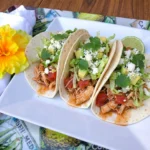 Three Crockpot Chicken Tacos filled with shredded chicken and fresh toppings