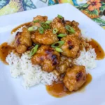 Crockpot Orange Chicken served over white rice with green onions and sesame seeds