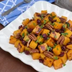 Maple Roasted Butternut Squash with Cranberries and toasted pecans in a white serving dish