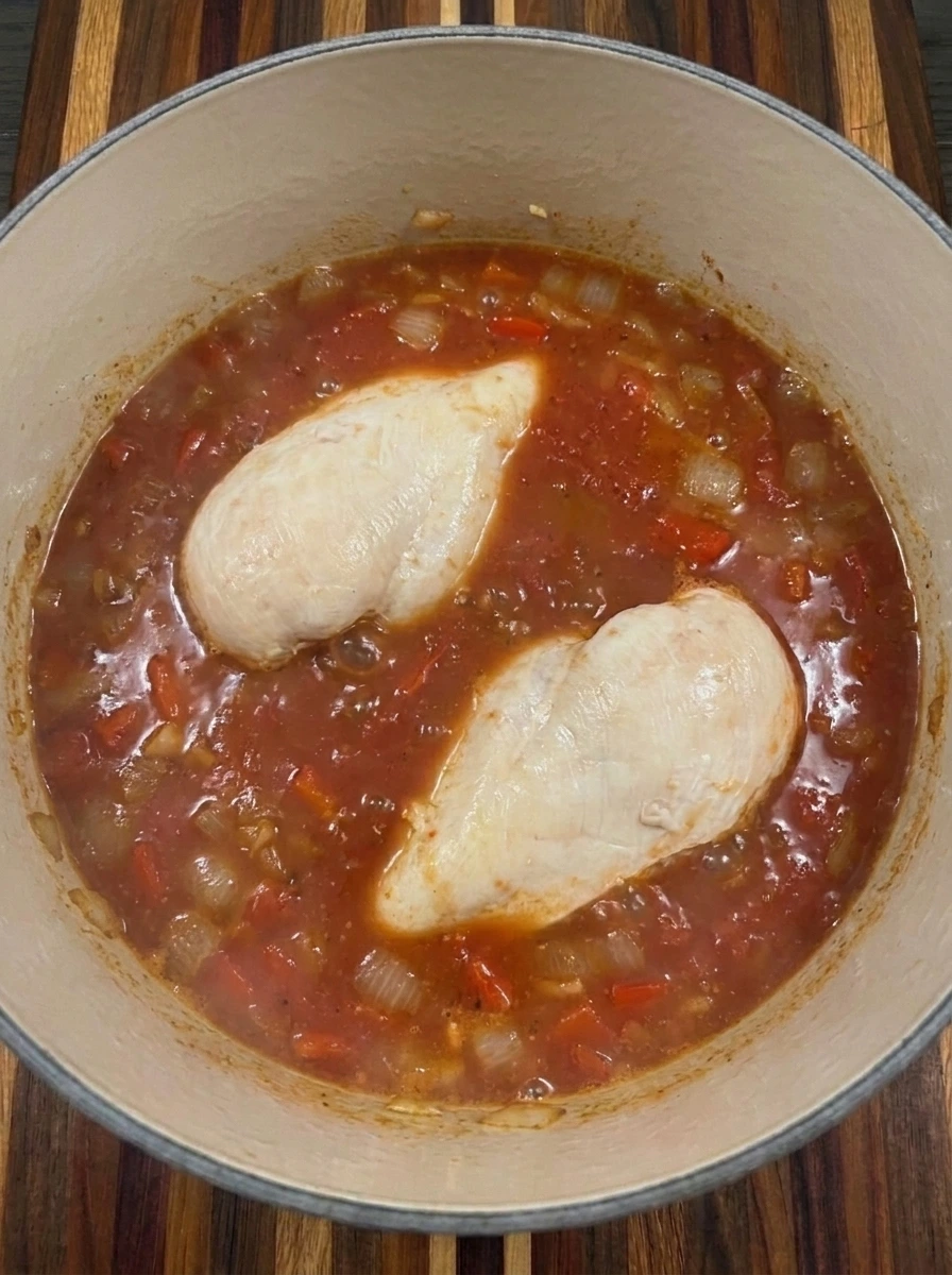 Two chicken breasts simmering in tomato broth with onion and red pepper