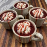 Four mugs of Vampire Hot Chocolate with whipped cream and strawberry syrup