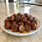 Homemade BBQ meatballs coated in glossy barbecue sauce with caramelized edges and fresh parsley on a white plate