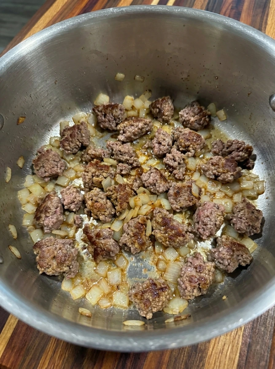 Ground beef browned with diced yellow onion in a large soup pot for cheesy beef and potato soup.