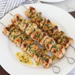 Golden Cowboy Butter Chicken Skewers coated in garlic herb butter and parsley on a white serving plate