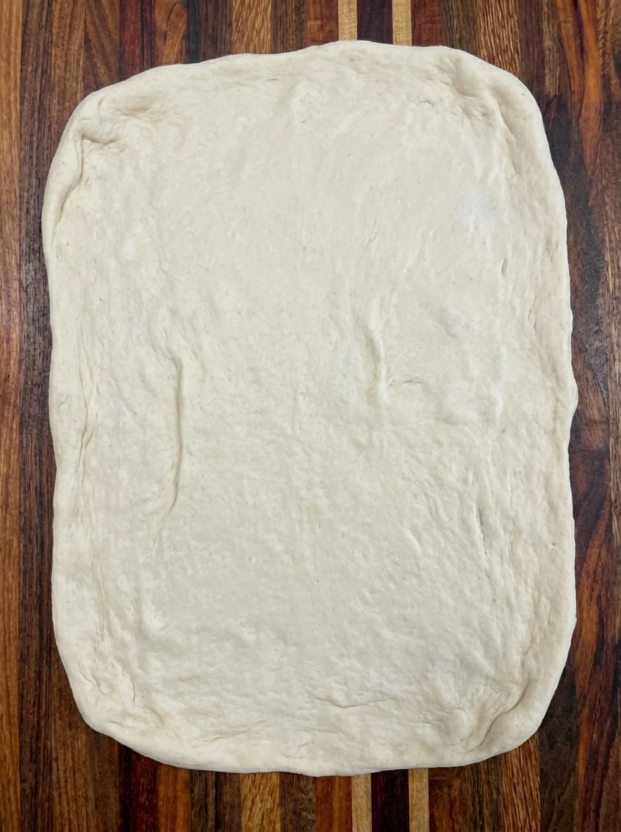 Raw pizza dough stretched into an uneven rectangle before making pepperoni breadsticks