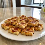 Golden Puff Pastry Pizza Bites topped with melted mozzarella and pepperoni on a white platter