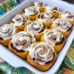 Homemade Pumpkin Cinnamon Rolls with golden brown swirls and cream cheese frosting in a ceramic baking dish