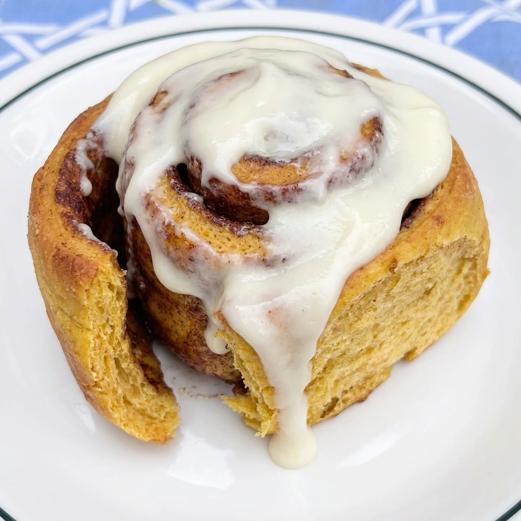 Single frosted pumpkin cinnamon roll on a white plate showing fluffy pumpkin dough and cinnamon layers