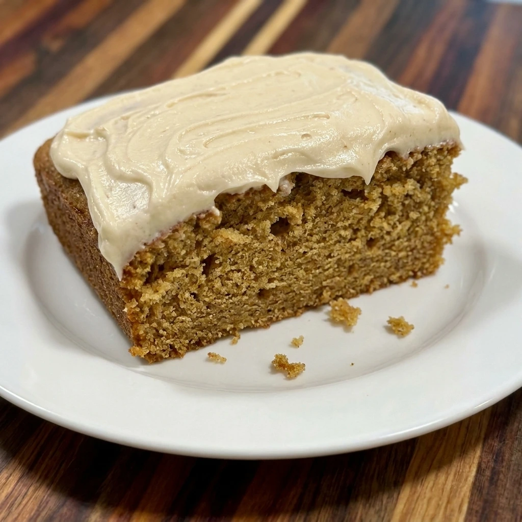 Single slice of moist spice cake with thick maple cream cheese frosting on a white plate.