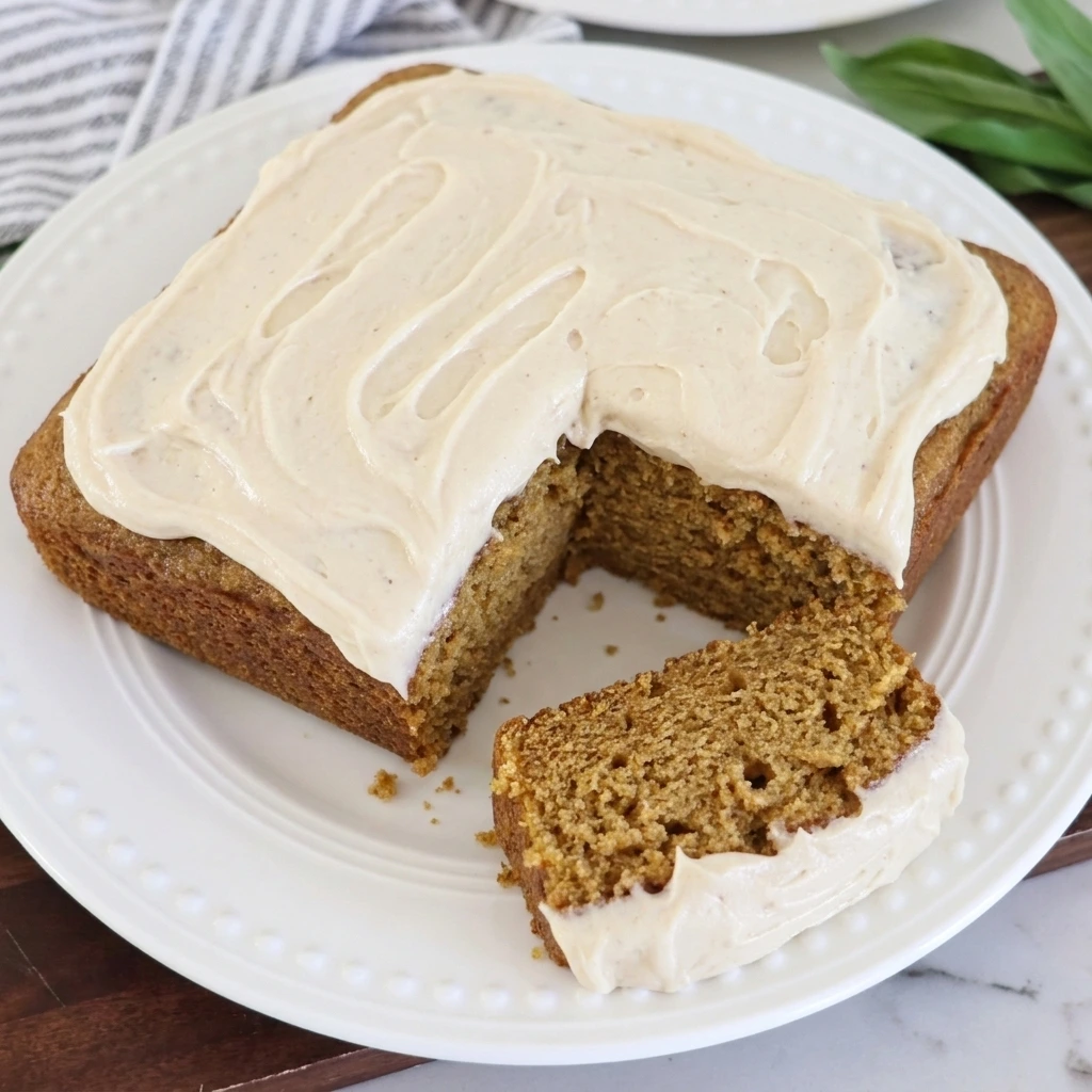 Homemade spice cake covered with maple cream cheese frosting and one cut slice showing the moist spiced crumb.