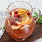 Homemade Thanksgiving Punch in a glass pitcher with apple cider and cranberry juice plus orange slices and apples and cranberries.