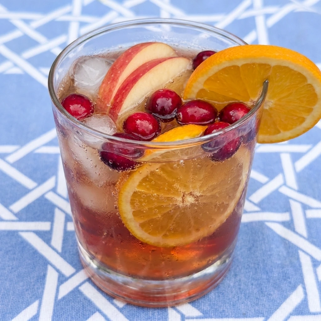 Single glass of Thanksgiving Punch with ice and apple slices and orange rounds and fresh cranberries.